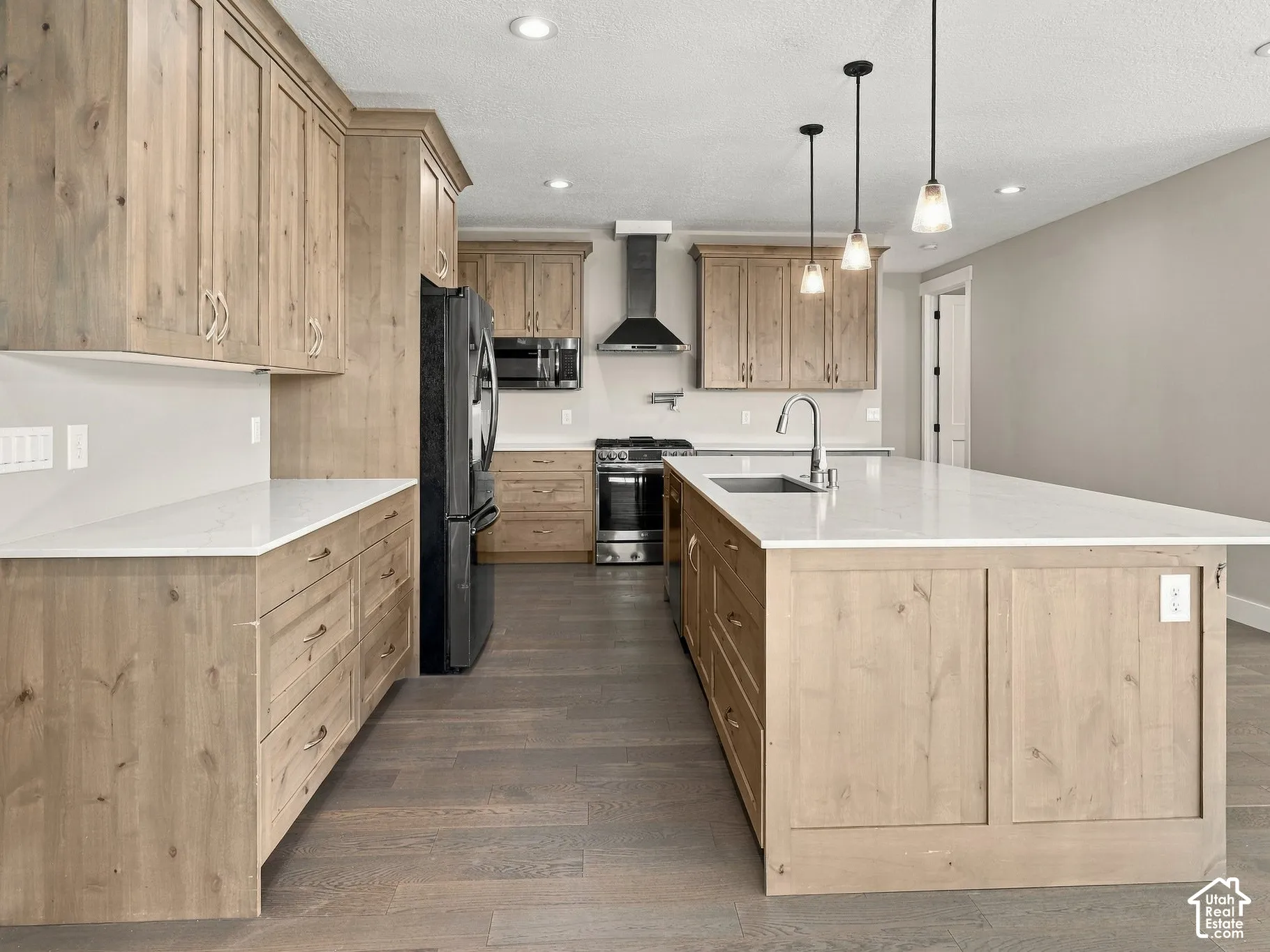 Kitchen featuring wood-finish cabinetry, quartz countertops, a central island with an undermount sink, stainless steel appliances, and pendant lighting