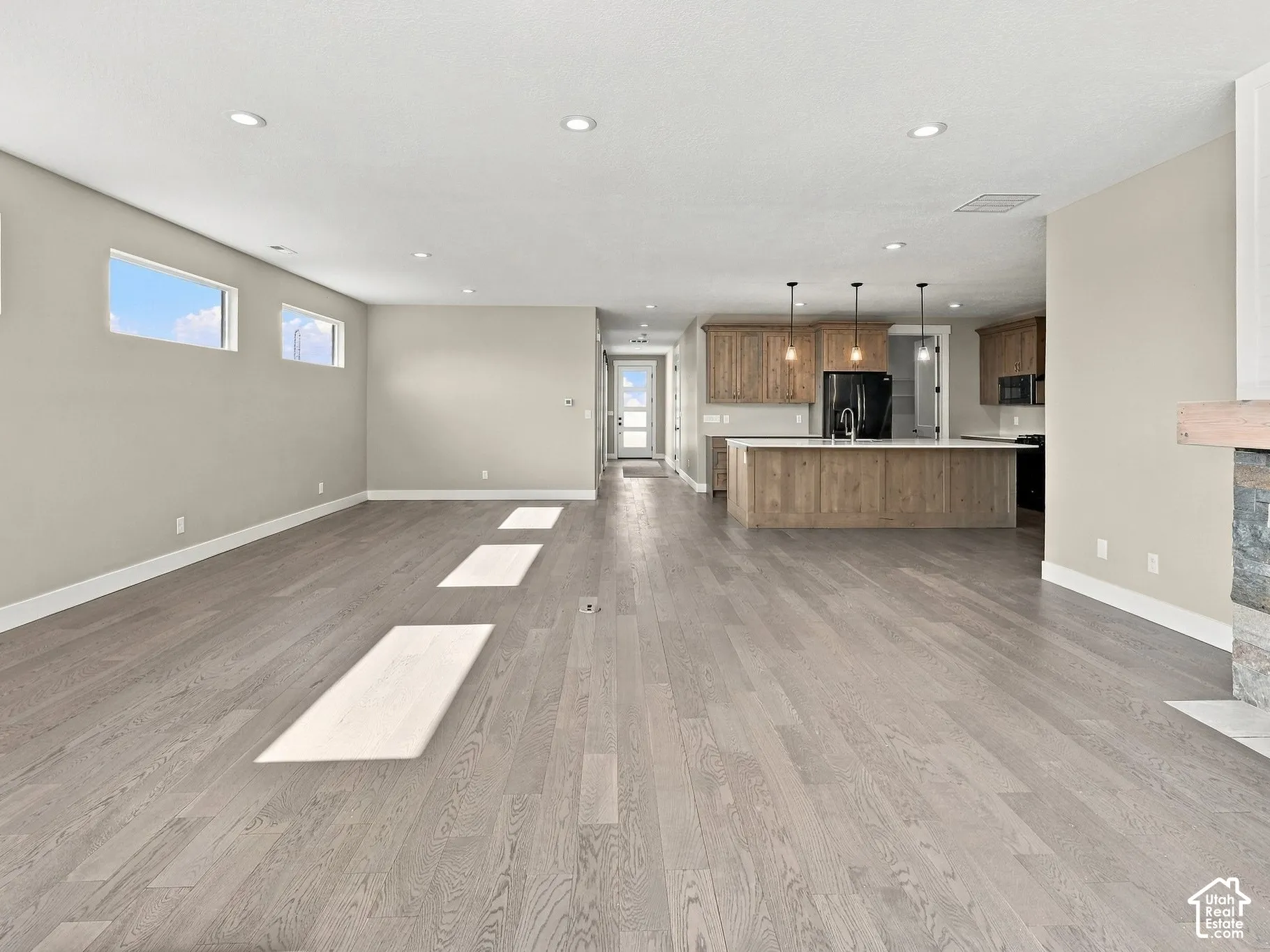 Open-concept living space featuring wood-finish flooring, recessed lighting, kitchen island with stone-finish countertops, and a fireplace with a stone surround and wood mantel