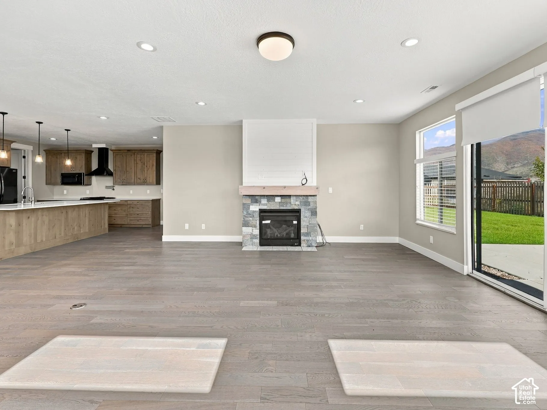 Open-concept interior featuring wood-finish flooring, a stone-surround fireplace with a mantel, quartz-topped kitchen island, recessed lighting, and sliding glass doors with mountain scenery