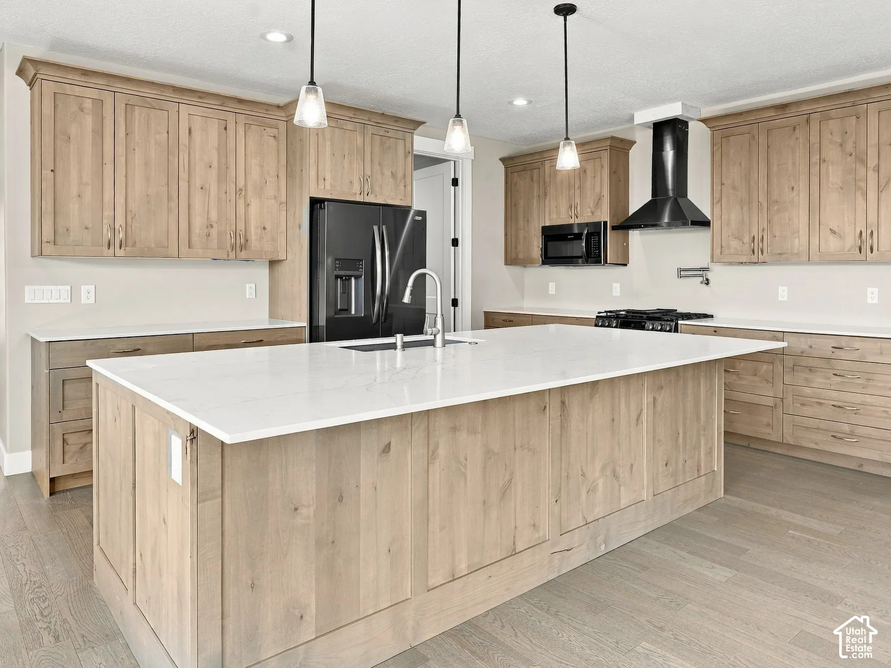 Kitchen featuring wood cabinetry, a large central island with quartz countertops, wood-finish flooring, three pendant lights, and a stainless steel wall-mounted pot filler