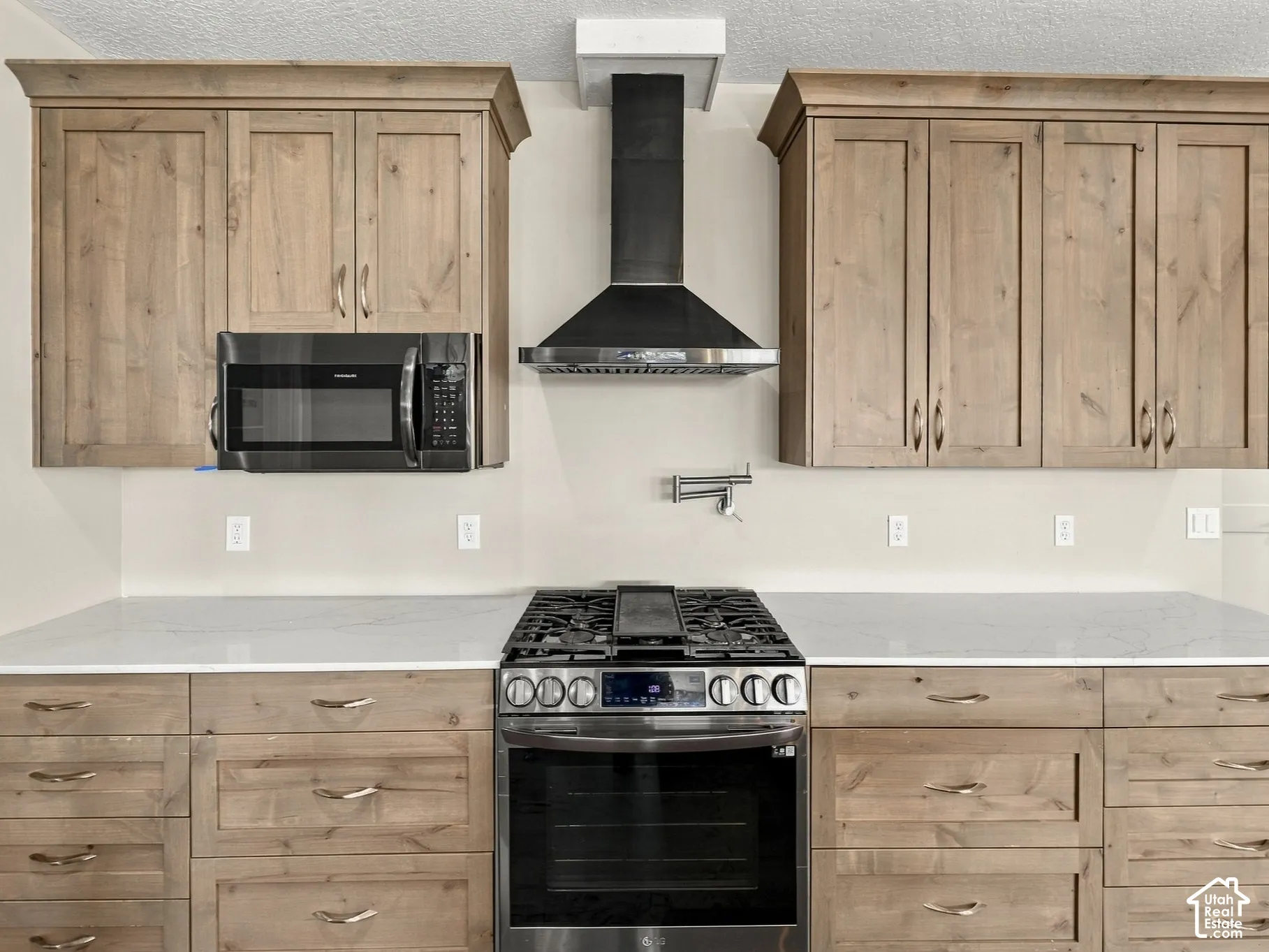 Kitchen featuring stained wood cabinetry with crown molding, light-toned stone countertops, a stainless steel gas range with a center griddle, an integrated microwave, and a wall-mounted pot filler faucet