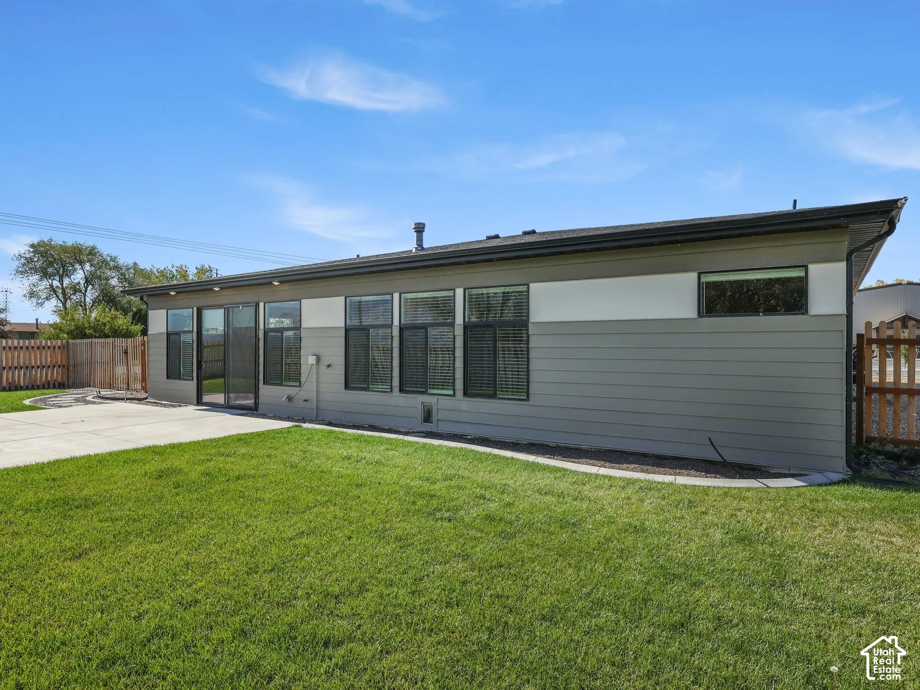 Exterior featuring horizontal siding with two-tone finish, concrete patio, expansive grass lawn, and wood privacy fencing