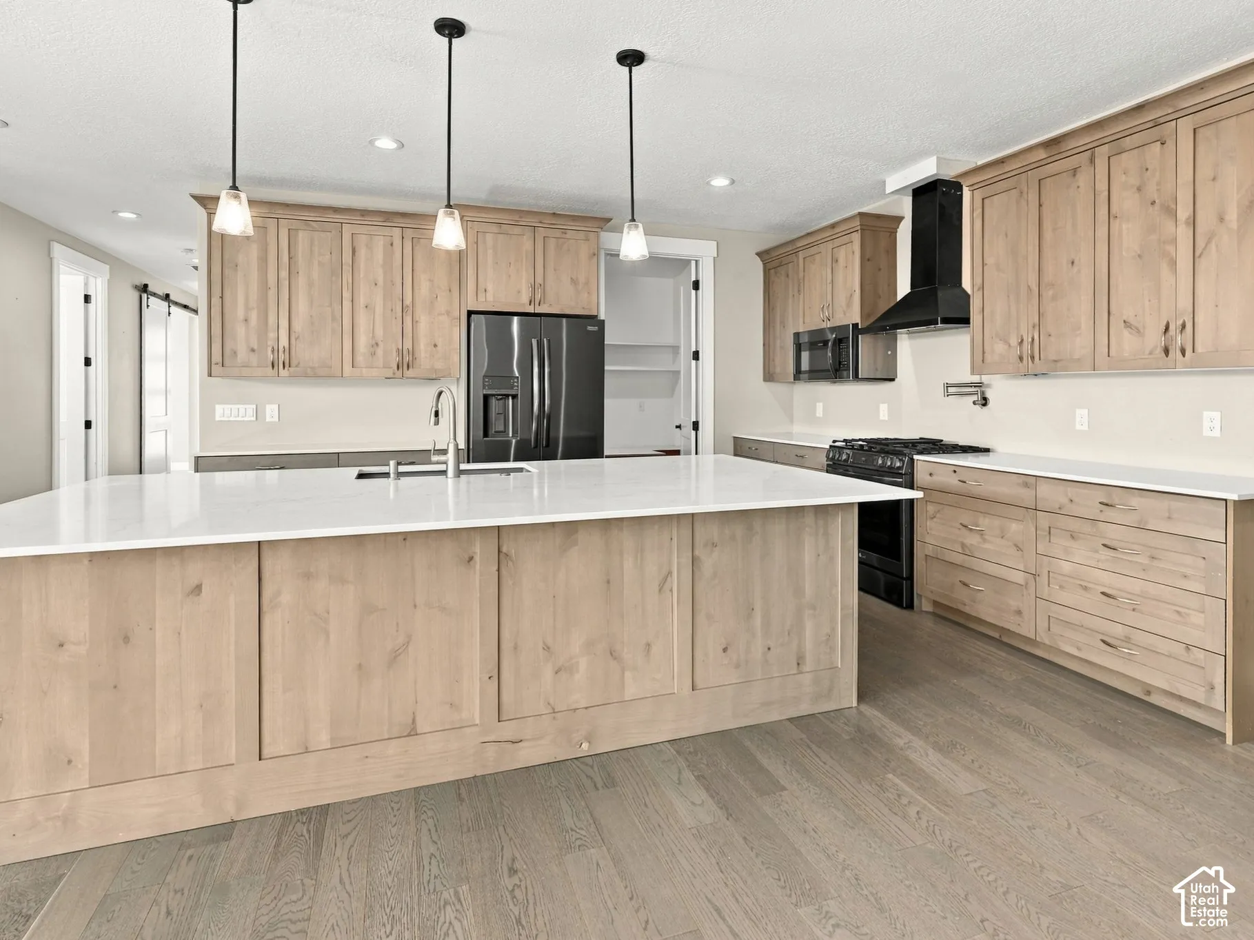 Kitchen featuring light wood-finish cabinetry, quartz countertops, a central island with an undermount sink, matte black appliances, and recessed lighting