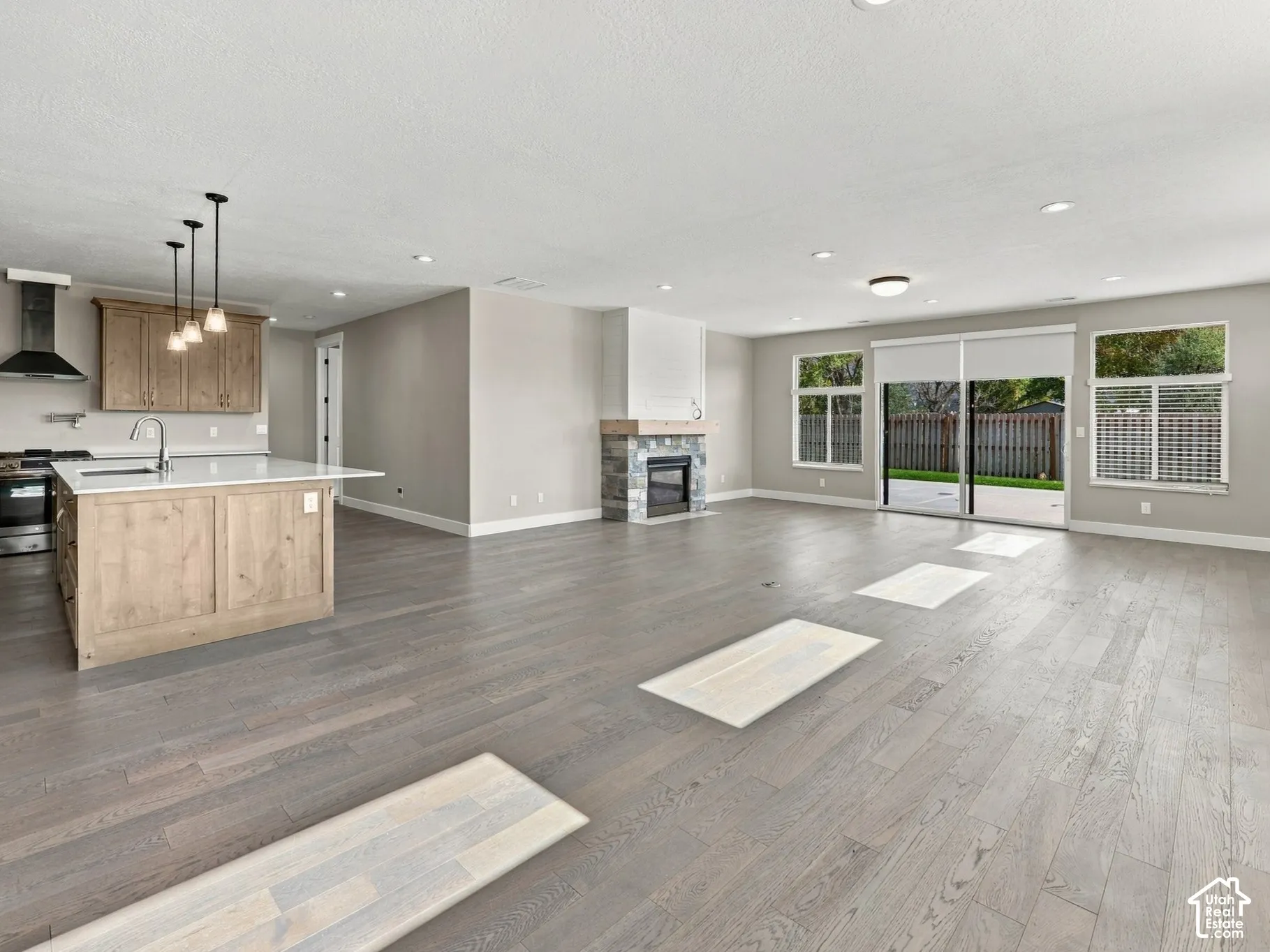 Open-concept space featuring wood-finish flooring, a kitchen island with quartz countertops, custom wood cabinetry, a stone-surround fireplace with a wood mantel, and glass sliding doors