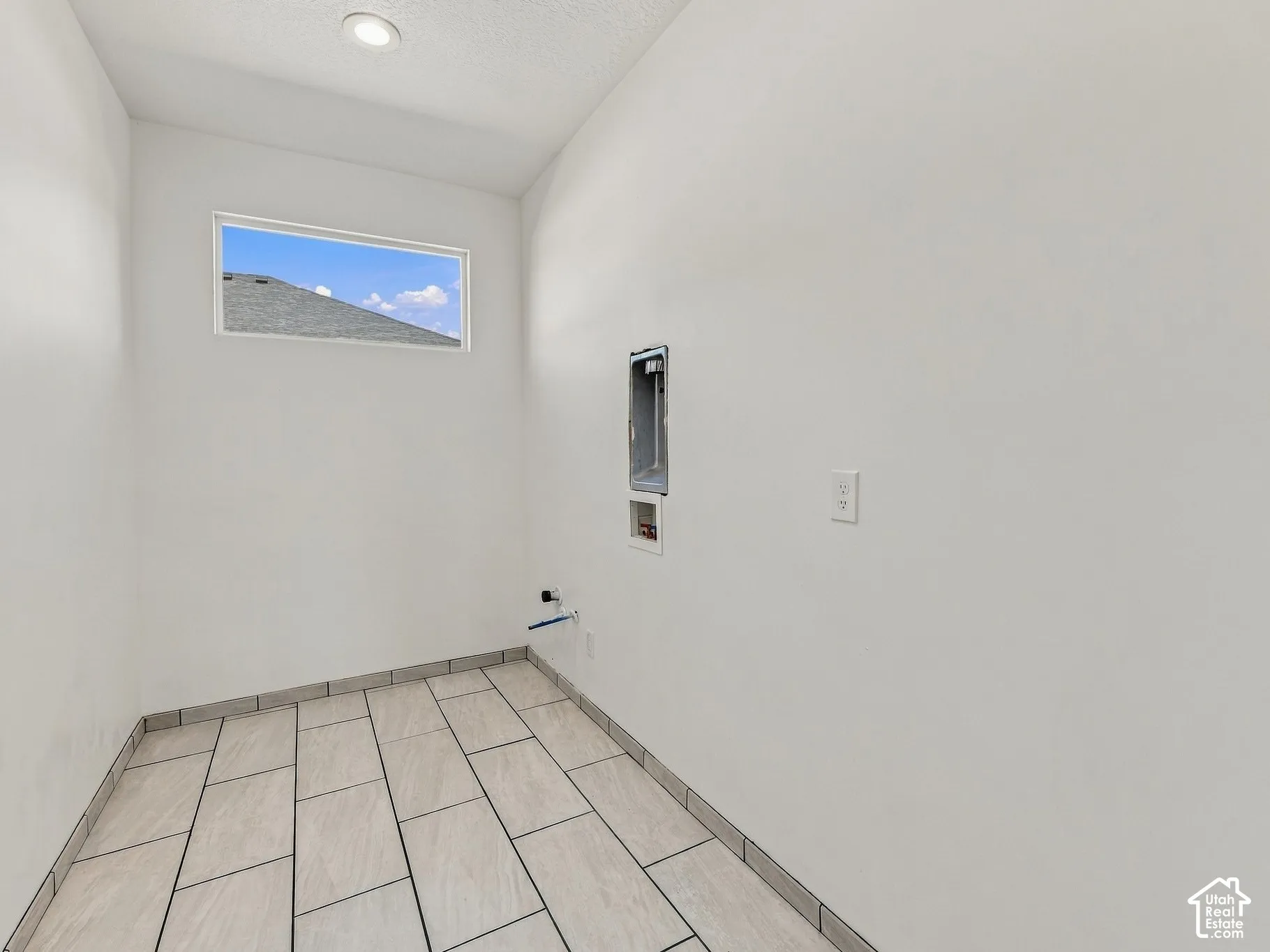 Utility space featuring large-format rectangular floor tile, recessed ceiling lighting, and a horizontal window
