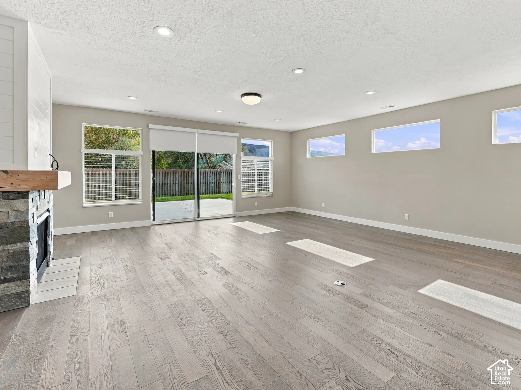 Spacious living area featuring wood-finish flooring, a stone-accented fireplace with a wood mantel, recessed lighting, and large sliding glass doors
