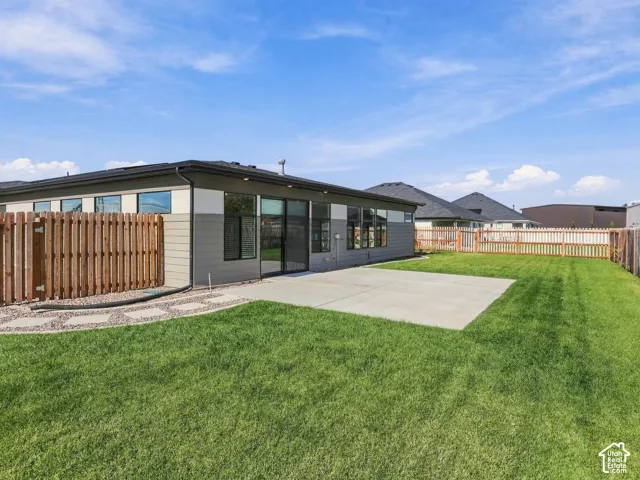 Rear exterior featuring a concrete patio, wood-style privacy fencing, and a manicured lawn