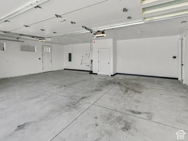 Three-car garage featuring a concrete floor, high ceilings with overhead door tracks, inset lighting, and multiple access doors