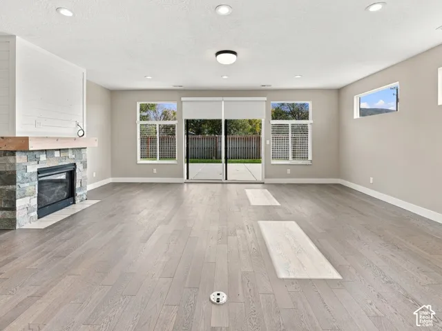 Living area featuring wood-finish flooring, recessed lighting, fireplace with stone surround and wooden mantel, horizontal shiplap accent, and glass sliding doors
