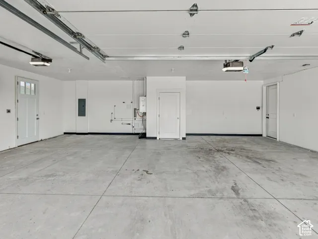 Finished multi-car garage featuring smooth concrete flooring, white walls, dual entry doors with glass paneling, and an integrated wall-mounted water heater