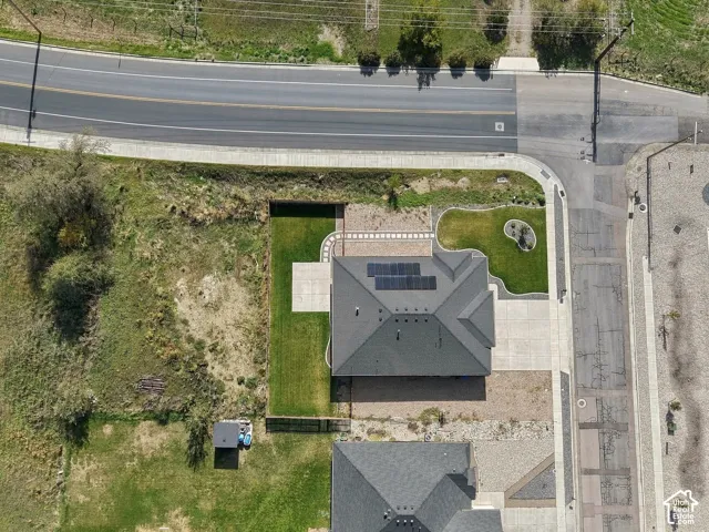 Corner lot featuring a concrete driveway, roof-mounted solar panels, paved walkway, manicured lawn, and hardscaped patio area