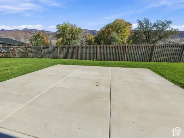 Backyard featuring a concrete patio, level lawn, wood-style privacy fencing, and mountain scenery