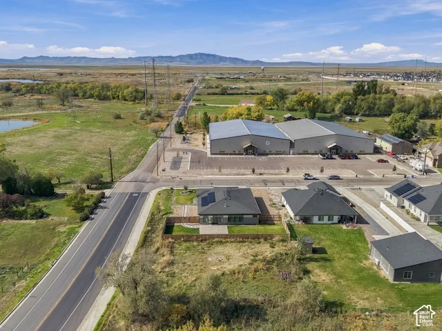 Aerial perspective featuring expansive land, paved parking areas, mountain backdrop, and multiple single-story structures with dark metal roofing
