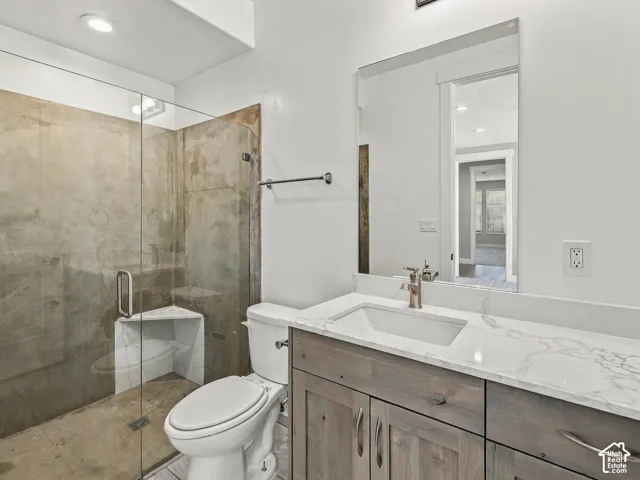 Bathroom featuring a vanity with a white countertop, wood-finish cabinetry, a glass-enclosed shower with a corner seat, and a rectangular undermount sink