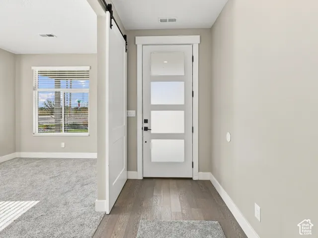 Entryway featuring a white exterior door with four glass panels, dark wood-finish flooring, and a white sliding barn door on a black track