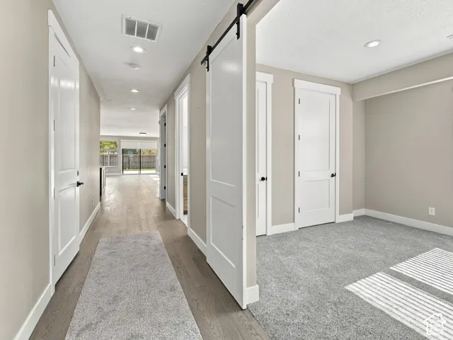 Hallway featuring wood-finish flooring, sliding barn door, recessed lighting, and wall-to-wall carpeting