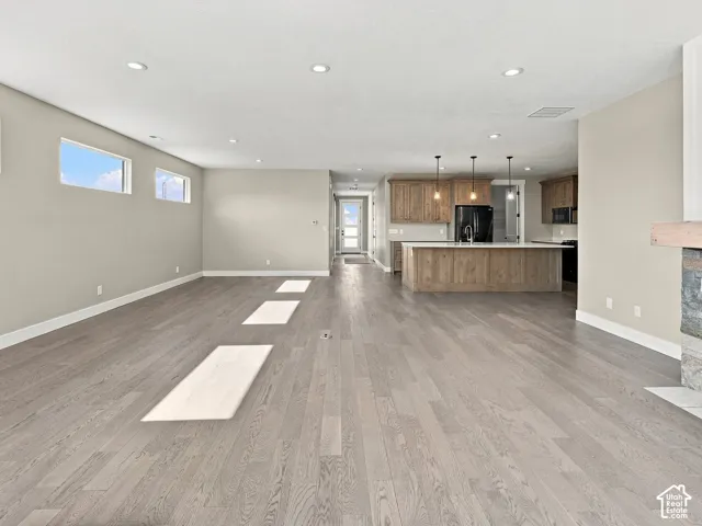 Open-concept living space featuring wood-finish flooring, recessed lighting, kitchen island with stone-finish countertops, and a fireplace with a stone surround and wood mantel