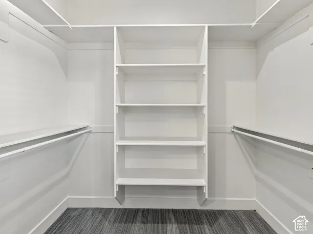Walk-in closet featuring white built-in shelving, dual hanging rods, and dark-toned flooring