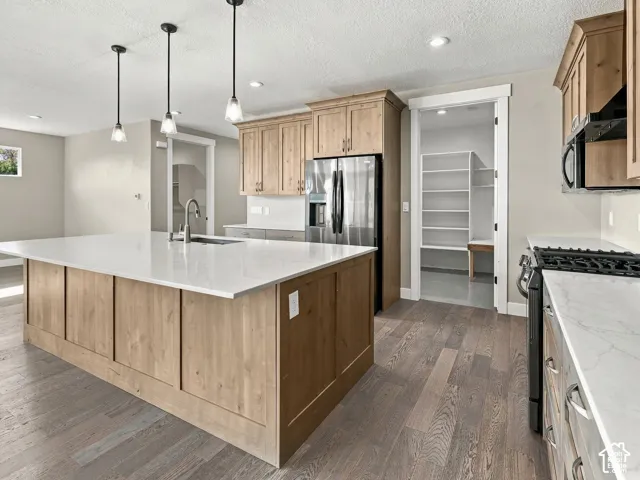 Kitchen featuring a central island with a quartz countertop, light-toned wood cabinetry, wood-finish flooring, three pendant lights, and a walk-in pantry