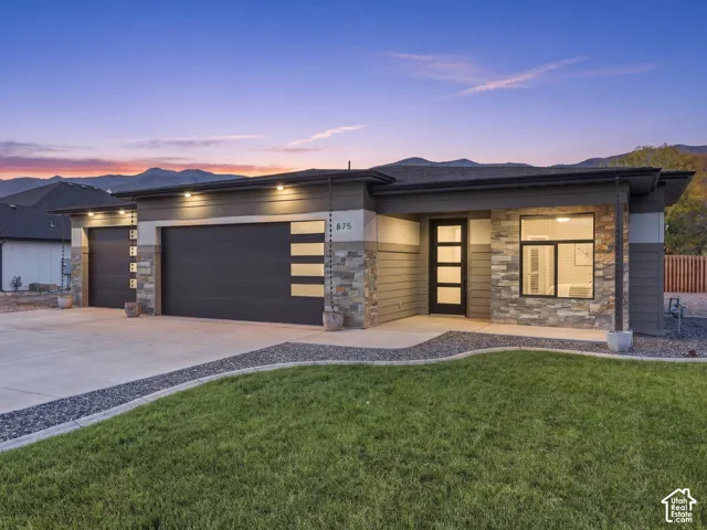 Contemporary exterior featuring stacked stone accents, horizontal siding, a multi-car garage with modern horizontal glazing, and an entrance with a multi-pane glass door, set against a mountain backdrop