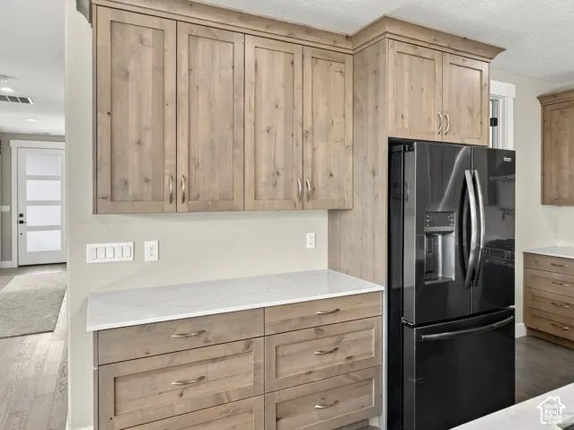 Kitchen featuring light wood-finish cabinetry, white stone-composite countertops, stainless steel hardware, and a black French-door refrigerator