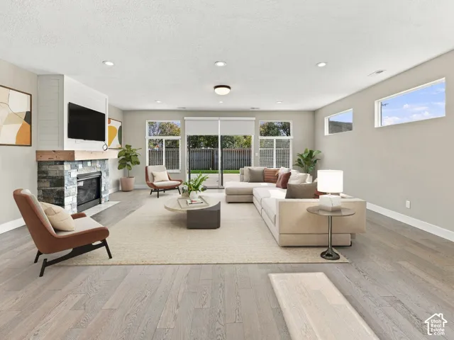 Open-concept living space featuring wood-finish flooring, recessed lighting, and a fireplace with stone facing and a horizontal wood mantel