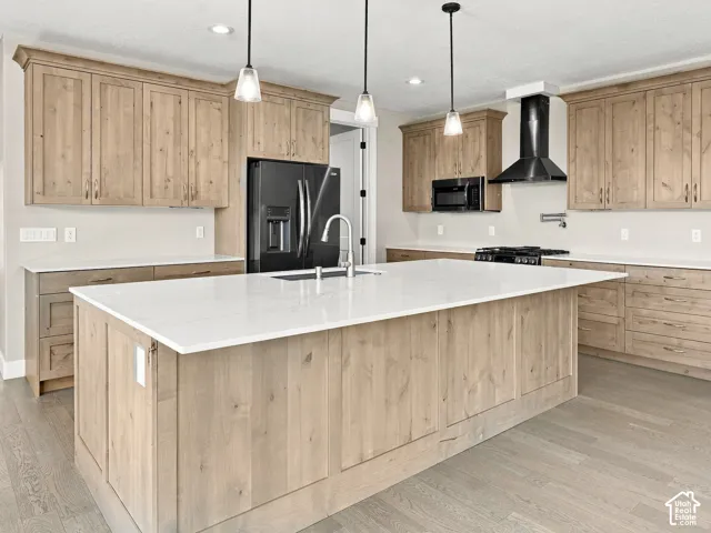 Kitchen featuring wood cabinetry, a large central island with quartz countertops, wood-finish flooring, three pendant lights, and a stainless steel wall-mounted pot filler