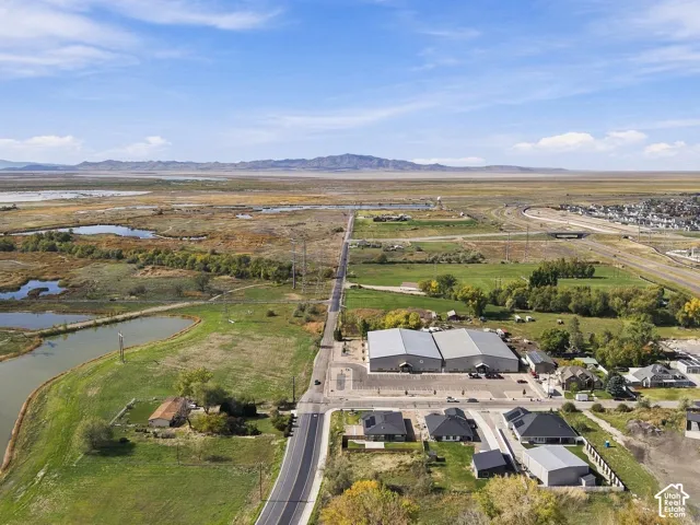 Aerial perspective of expansive acreage featuring dual industrial-style structures, asphalt-paved parking, natural ponds, and mountain scenery