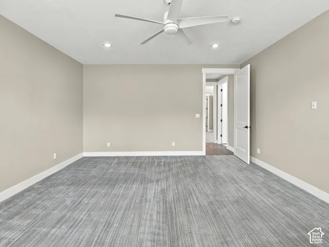 Neutral-toned walls, grey textured carpeting, white panel door, and ceiling fan with integrated lighting