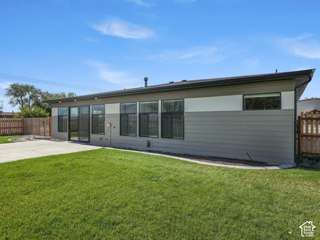 Exterior featuring horizontal siding with two-tone finish, concrete patio, expansive grass lawn, and wood privacy fencing