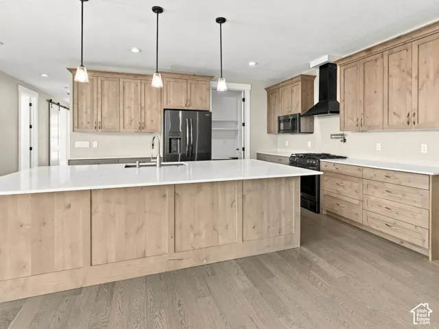 Kitchen featuring light wood-finish cabinetry, quartz countertops, a central island with an undermount sink, matte black appliances, and recessed lighting