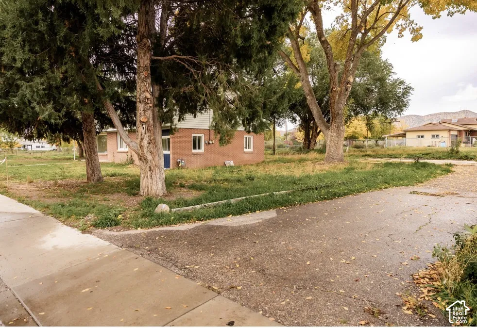 Brick exterior featuring mature trees, concrete driveway, and mountain backdrop