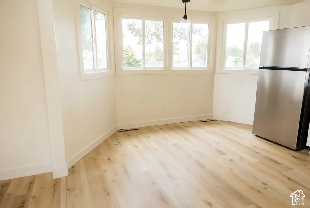 Light-filled area featuring wood-finish flooring, sliding windows, a pendant light fixture, and a stainless steel refrigerator