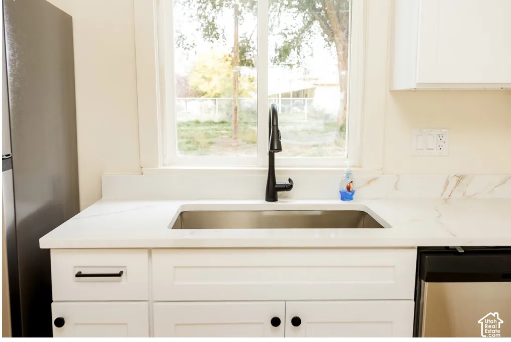 Kitchen sink featuring a stainless steel basin, matte black high-arch faucet, stone-finish countertops with integrated backsplash, white shaker-style cabinetry, and metallic hardware