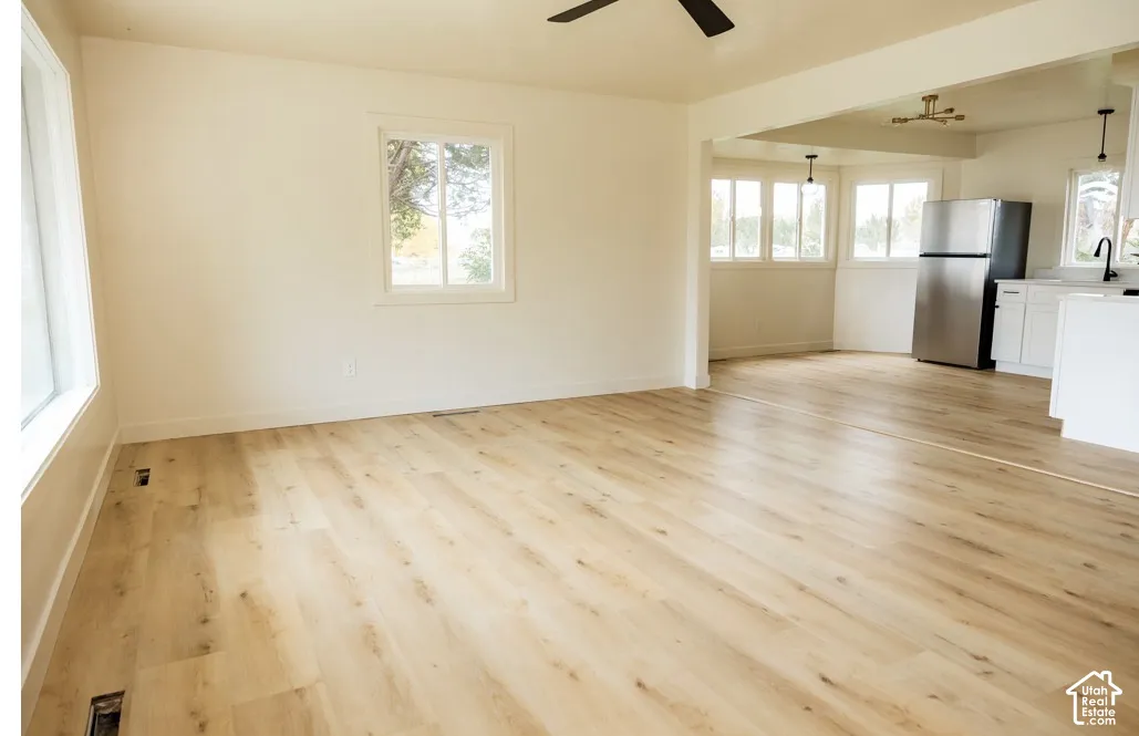 Open floor plan featuring light wood-finish flooring, white cabinetry, stainless steel refrigerator, and large windows