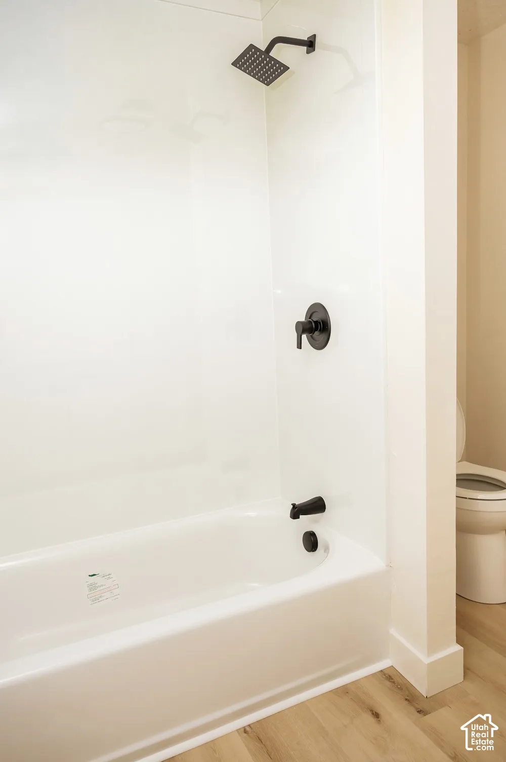 Bathroom featuring a white acrylic bathtub surround, matte black rainfall shower head, matte black wall-mounted faucet, and wood-finish flooring