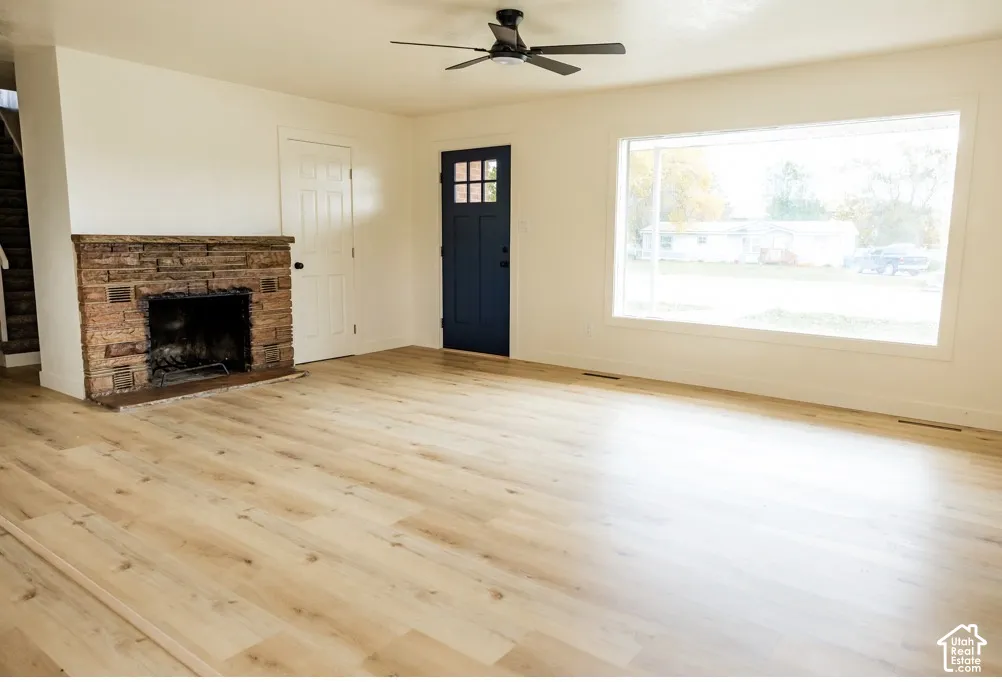 Living area featuring light-toned wood-finish flooring, a masonry fireplace, a large picture window, and a Craftsman-style door