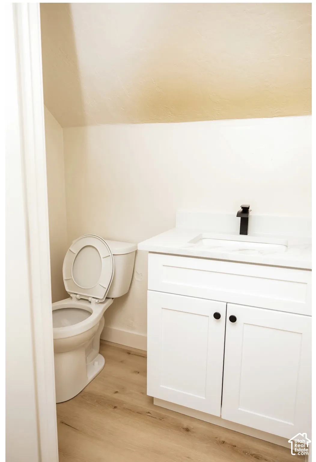 White vanity with shaker-style cabinetry, matte black hardware, rectangular undermount sink, matching matte black faucet, and wood-finish flooring