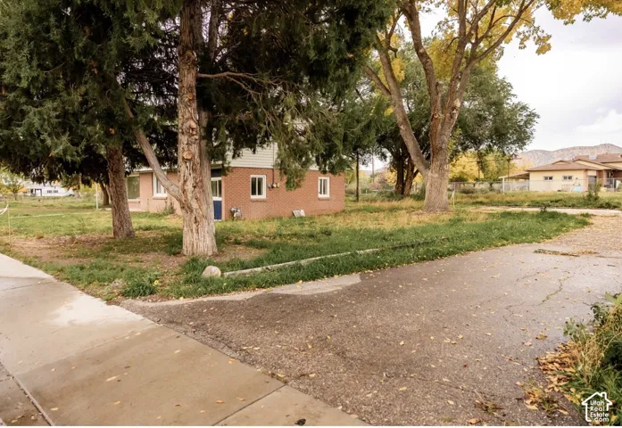 Brick exterior featuring mature trees, concrete driveway, and mountain backdrop