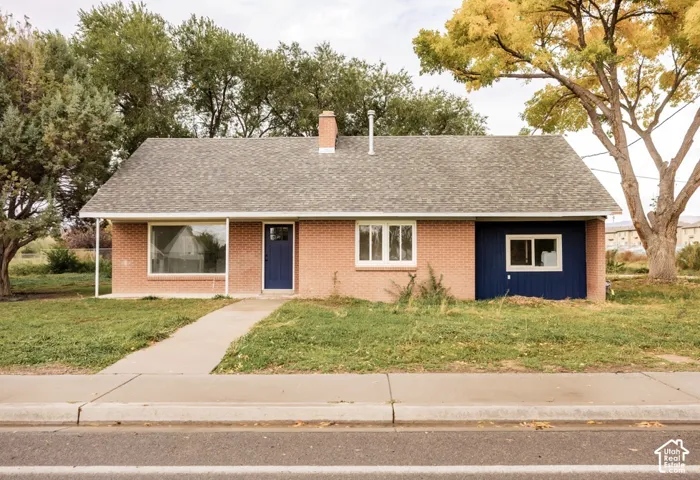 Single-story brick exterior featuring a shingle roof, chimney, blue accent siding, and large picture windows