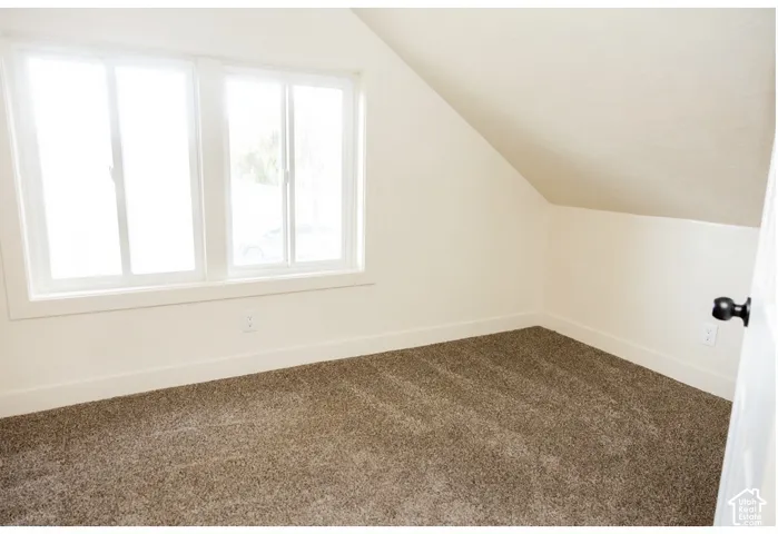 Neutral-toned interior space featuring vaulted ceilings, dual-pane sliding windows, and wall-to-wall carpeting