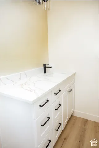 White cabinetry vanity featuring a stone-surface countertop, integrated rectangular sink, matte black hardware, and matching black faucet, complemented by wood-finish flooring