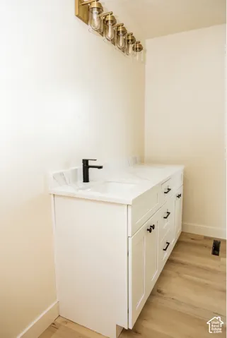 White vanity featuring a stone-look countertop, integrated rectangular sink, matte black faucet, and matte black cabinet hardware, complemented by a gold-tone multi-bulb light fixture and wood-finish flooring