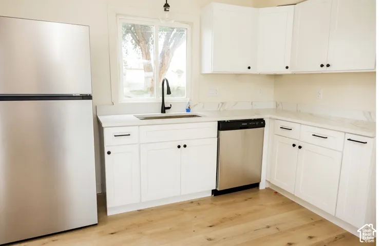 Kitchen featuring white shaker-style cabinetry, light-toned stone-patterned countertops, stainless steel appliances, wood-finish flooring, and a matte black gooseneck faucet