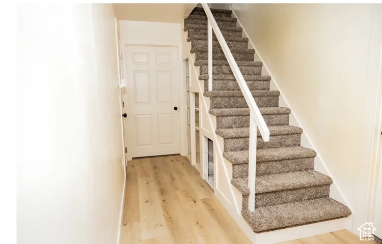 Staircase with carpeted treads, white handrail, and integrated under-stair storage shelving, featuring wood-finish flooring and a six-panel door
