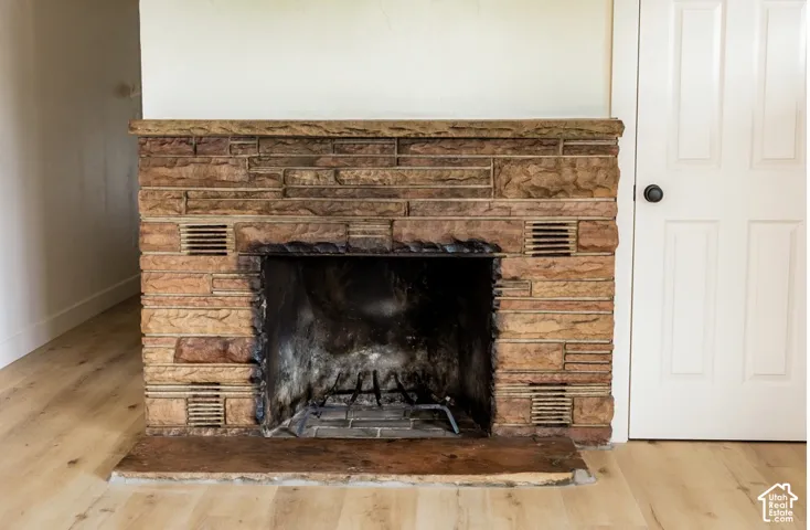 Floor-to-ceiling stone fireplace featuring a textured hearth, integrated masonry mantel, and wood-finish flooring