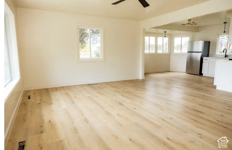Open floor plan featuring light wood-finish flooring, white cabinetry, stainless steel refrigerator, and large windows