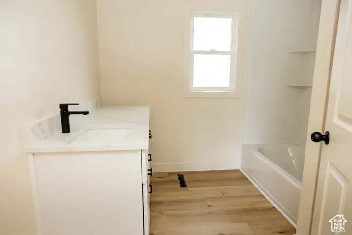 White vanity with integrated basin and stone-finish countertop, matte black faucet, and wood-finish flooring