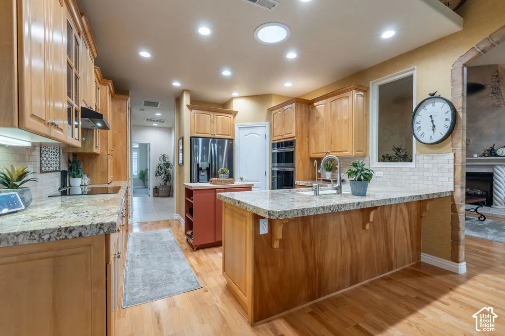 Kitchen featuring light wood cabinetry, stone countertops, stainless steel double wall ovens, a central island with decorative corbels, and recessed lighting
