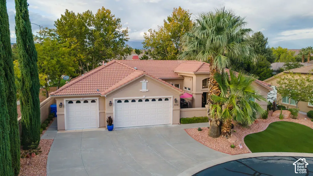 Stucco exterior with a tiled roof, three-car garage, mature palm trees, and professional xeriscape landscaping